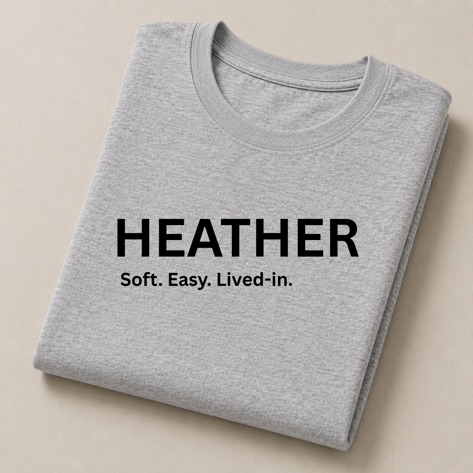 A folded light heather gray T-shirt with black printed text reading 'HEATHER Soft. Easy.